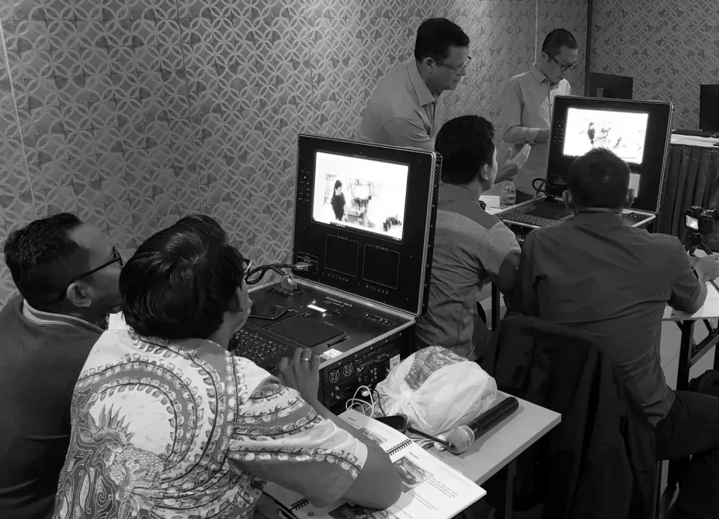 A group of men in a seminar room focusing on screens displaying x-ray images. The atmosphere is studious and collaborative, with patterned walls.