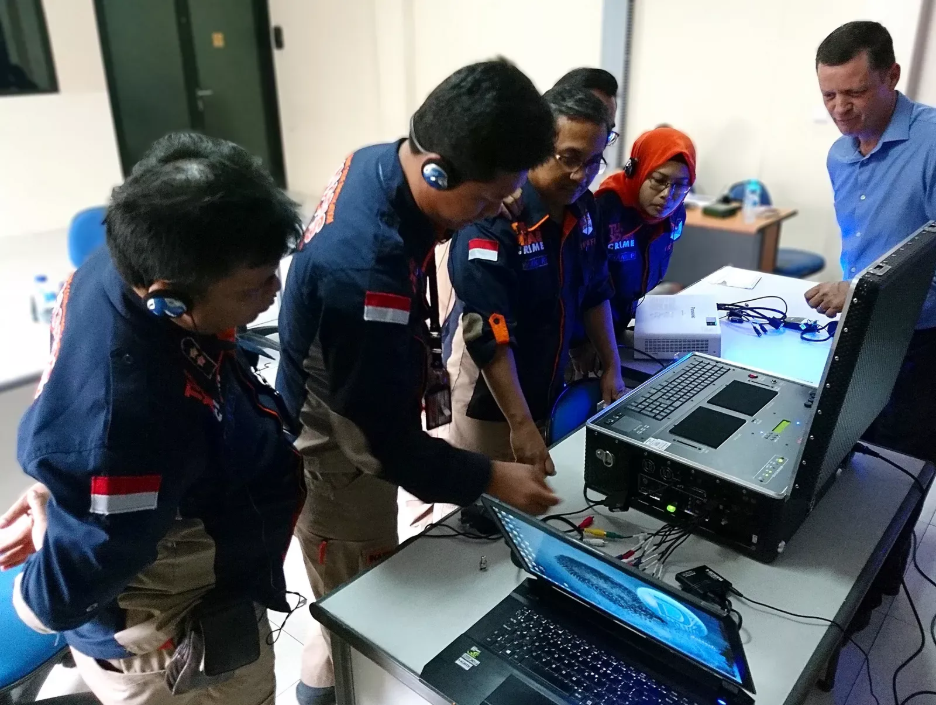Team of technicians examining surveillance equipment and laptop in a lab setting.